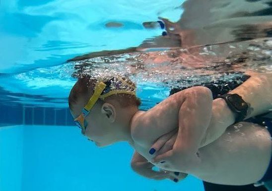 A baby practicing in the water with an adult